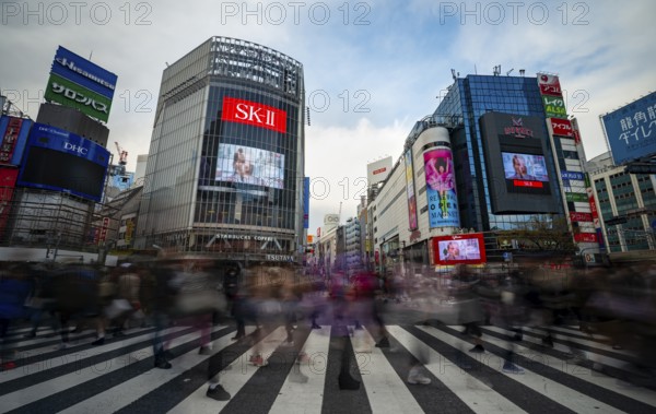 Crowd crossing zebra crossings on a large intersection, motion blur, modern houses with colorful neon signs at the back, long exposure Hibuya Crossing, Shibuya, Tokyo, Japan