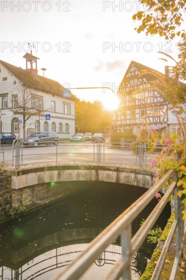 Bridge over a river, half-timbered buildings at sunset, autumn trees next to the road, Aidlingen, Böblingen district, Germany