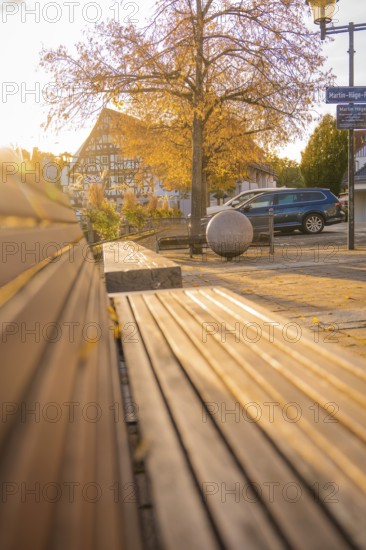 Empty wooden bench in a sunlit village square with half-timbered house in the background, Aidlingen, Böblingen district, Germany