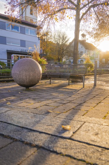 Bench next to a big ball, long shadows at sunset, autumnal town square, Aidlingen, Böblingen district, Germany