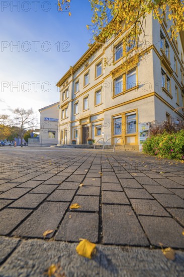 Two-story building with autumn leaves on the forecourt, under blue sky, Aidlingen, Böblingen district, Germany