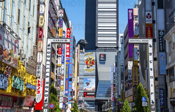 Bustling street scene in Japan with modern buildings and colorful billboards, figure of Godzilla head on a high-rise building, Shinjuku City, Tokyo, Japan