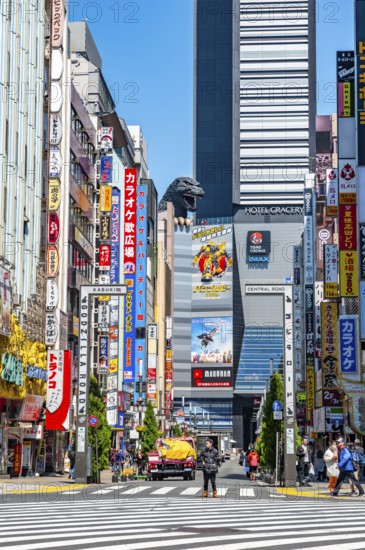 Bustling street scene in Japan with modern buildings and colorful billboards, figure of Godzilla head on a high-rise building, Shinjuku City, Tokyo, Japan