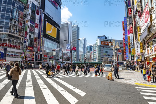 Large intersection with billboards and colorful signs at shops and restaurants, busy downtown with high-rise buildings, Shinjuku City, Tokyo, Japan
