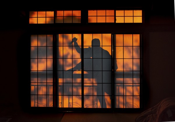 Shadow of a man climbing over balcony railings, burglar with knife, assassin, ninja, on the balcony behind a shoji sliding door in a traditional Japanese house, Yamanouchi, Nagano, Japan