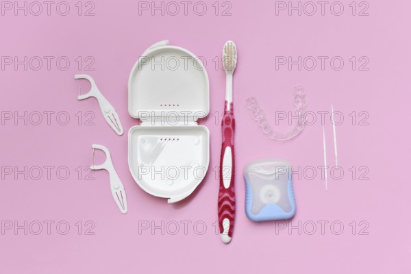 Top view of dental clear aligners, toothbrush, toothpicks and floss on pink background with copy space
