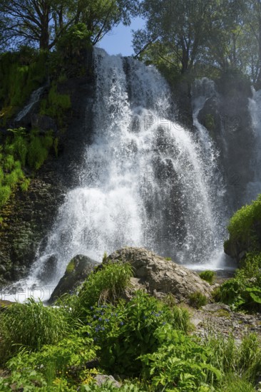 A waterfall falls over several rocks surrounded by lush vegetation under a blue sky, Shaki Waterfall, Syunik Province, Syunik, Armenia
