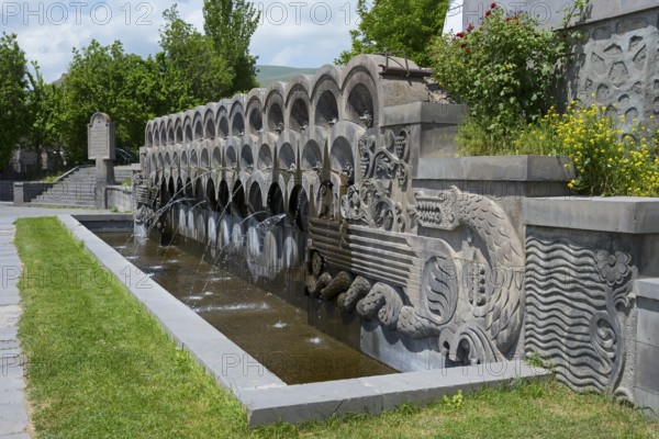 Stone fountain with sculptures surrounded by plants in bright weather, monument to the 40th anniversary of the victory in the Great Patriotic War, Sisian, Sisian, Syunik province, historically Sangesur, Armenia