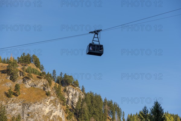 A Tegelbergbahn cabin floats over a mountainous landscape under a clear blue sky, near Schwangau, Ostallgäu, Allgäu, Bavaria, Germany