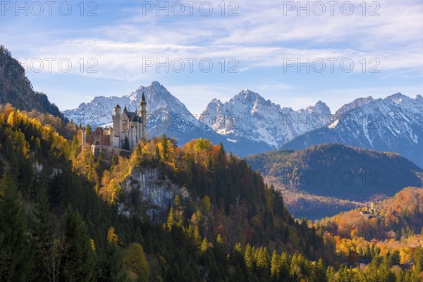 Neuschwanstein Castle in a forest of colorful autumn trees, against snow-covered mountains and blue skies, Schwangau near Füssen, Ostallgäu, Allgäu, Bavaria, Germany