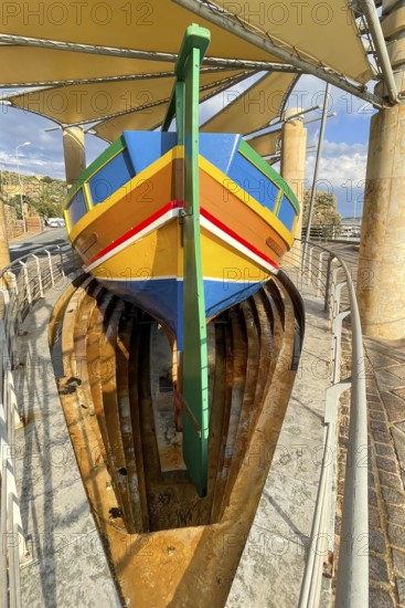 Monument to traditional fishing boats abandoned jacked up typical colorful painted old fishing boat with large rudder blade at the stern of Gozo at Gozo harbour, Mgarr Harbour, Gozo, Malta