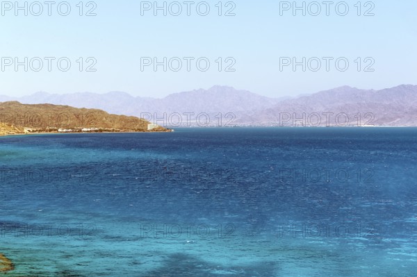 View of the Egyptian coast from the Sinai peninsula not far from the border with Israel across turquoise blue water from in the Gulf of Aqaba Red Sea on the Jordan coast with a small city of Aqaba in the background, Egypt, Jordan