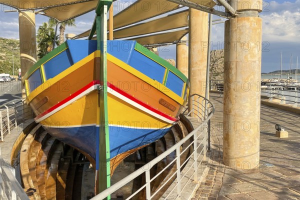 Monument to traditional fishing boats abandoned jacked up typical colorful painted old fishing boat with large rudder blade at the stern of Gozo at Gozo harbour, Mgarr Harbour, Gozo, Malta