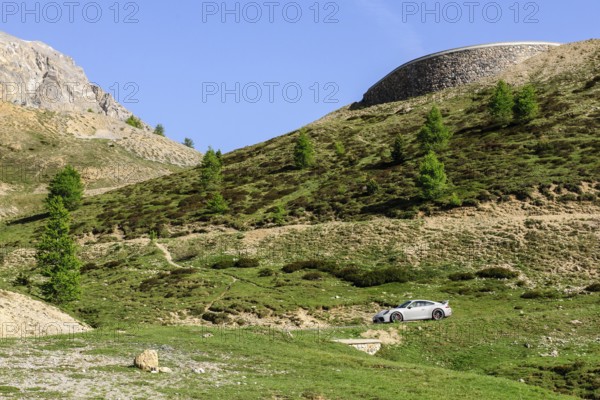 Porsche GT3 sports car drives on mountain road above tree line Col de d' Izoard l' Izoard l'Izoard in the high Alps, department of Auvergne-Rhône-Alpes, France