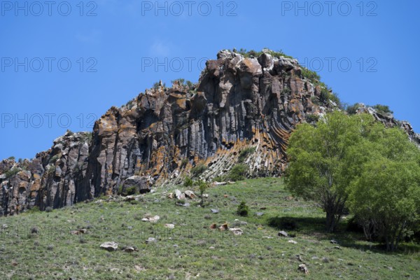 Mighty rock formation with lush greenery and clear skies, radiating peace and natural beauty, basalt columns near Shaki Waterfall, Syunik Province, Armenia