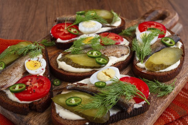 Sandwiches on rye bread with sprats, quail eggs, fresh tomatoes and pickled cucumber, on a wooden board, appetizer, breakfast