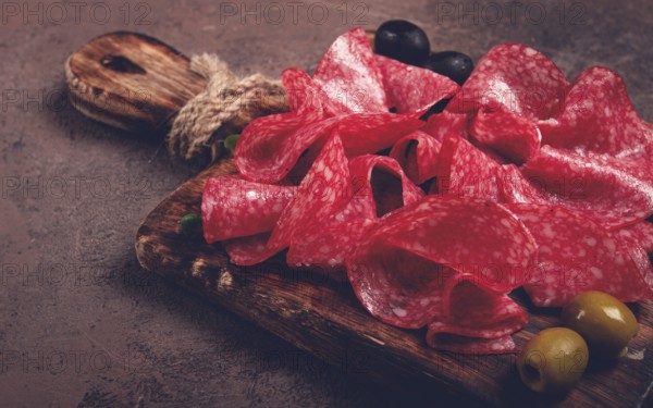 Sliced salami sausage, on a wooden chopping board, decorated with olives and herbs, close-up, no people