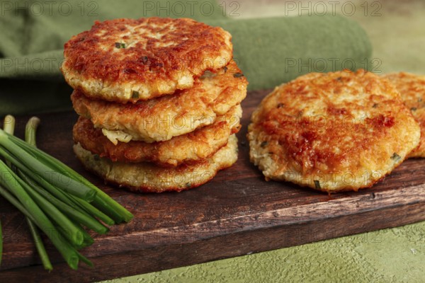 Crispy potato pancakes Latkes, stacked on a wooden board next to fresh green onions, natural light, homemade, no people