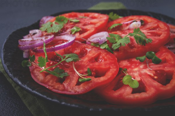 Freshly sliced tomatoes and red onions, garnished with herbs, on a black plate, summer salad, no people