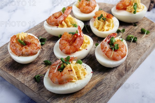 Boiled eggs stuffed with yolk and seasoned with mayonnaise, stuffed eggs with shrimp, on a wooden chopping board, selective focus, close-up, no people