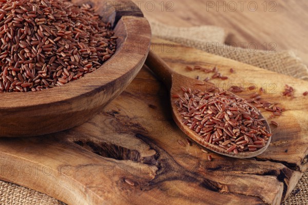 Natural, red rice, in a wooden bowl and spoon on a wooden surface in rustic style, top view