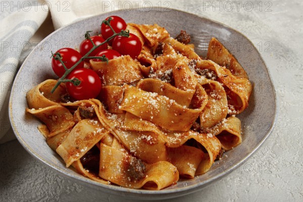 Pappardelle pasta with bolognese sauce, topped with parmesan cheese and cherry branch, homemade, no people