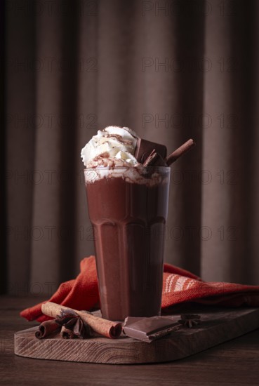 Hot chocolate drink, topped with whipped cream, chocolate shavings, and a cinnamon stick