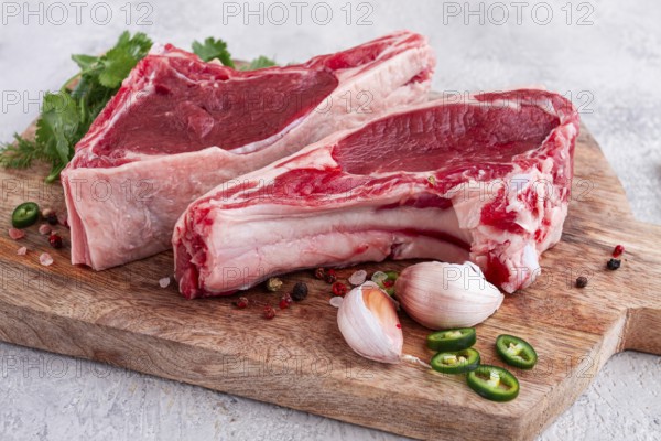 Fresh pieces of beef on the bone, on a wooden cutting board, with herbs and spices, ready for cooking in the kitchen
