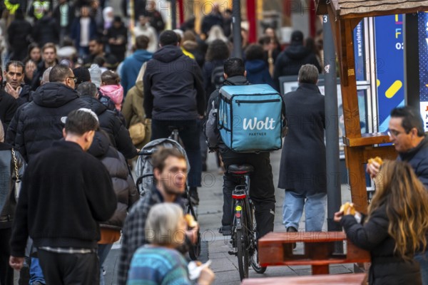 Full city center, shopping street, Kettwiger Straße pedestrian zone in Essen, bicycle courier from the Wolt delivery service crowds through the many people in front of the opening of the Christmas market, North Rhine-Westphalia, Germany