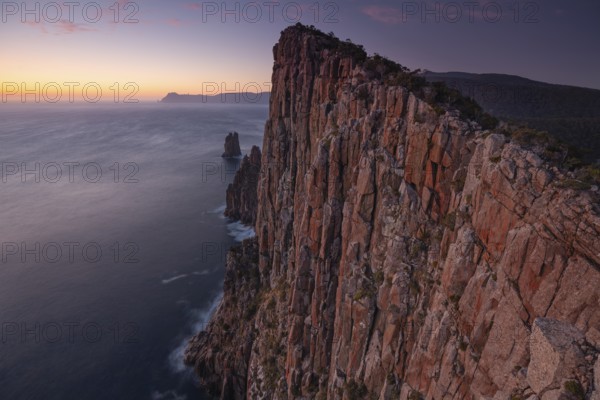 Long exposure at sunrise shows the glowing dawn over the huge rocks of Cape Hauy. Waves hit the steep cliffs. Cape Hauy, Tasman Peninsula, Tasmania, Australia