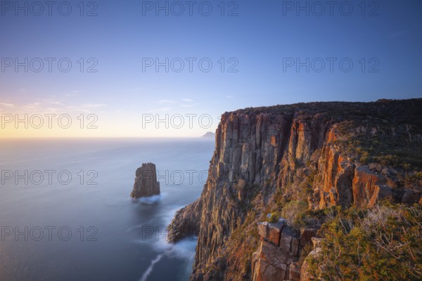 Long exposure at sunrise shows glowing dawn over the dramatic cliffs of Cape Hauy. View towards Cape Pillar. Gentle waves hit the steep cliffs. Cape Hauy, Tasman Peninsula, Tasmania, Australia