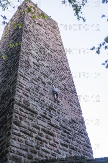 A climber climbs the stone wall of a tower, accentuated by clear air and natural surroundings, Mandelberg Castle Ruins, Pfalzgrafenweiler, Freudenstadt District, Germany