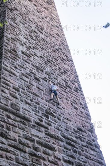 A climber climbs a massive stone tower surrounded by trees and blue sky, Mandelberg Castle Ruins, Pfalzgrafenweiler, Freudenstadt District, Germany