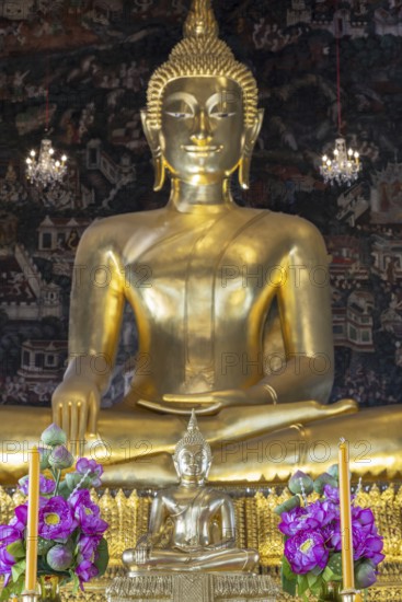 Golden Buddha statue, Phra Buddha Trilokachet surrounded by crystal chandeliers and exquisite wall paintings, interior view of Phra Ubosot or ordination hall, Wat Suthat Thepwararam, Royal Temple, Phra Nakhon, Bangkok, Thailand