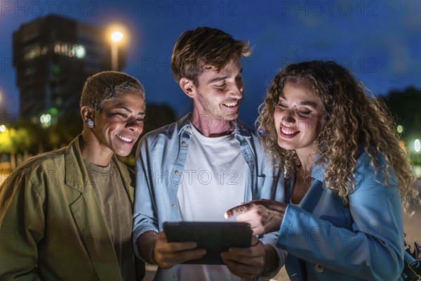 Diverse young friends gathering closely, smiling and interacting with a glowing digital tablet on a city street at night, symbolizing connection, friendship, and urban technology use