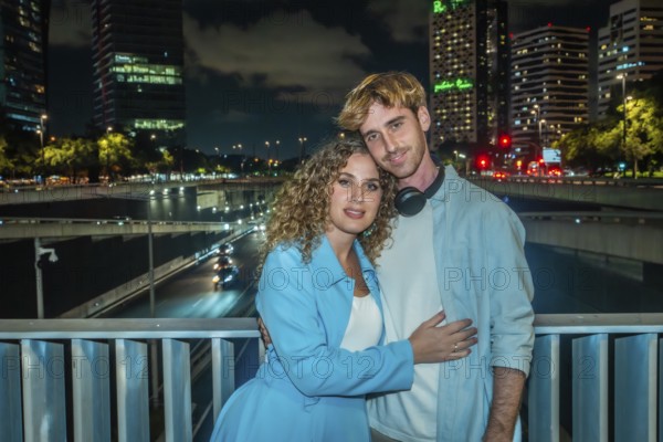 Young couple embracing on an urban bridge at night, city skyline and streaking highway lights forming a vibrant modern backdrop for romance and togetherness