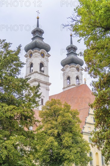 Two decorative church towers rise above a red roof surrounded by green trees, ZFP Zwiefalten, Reutlingen district, Germany