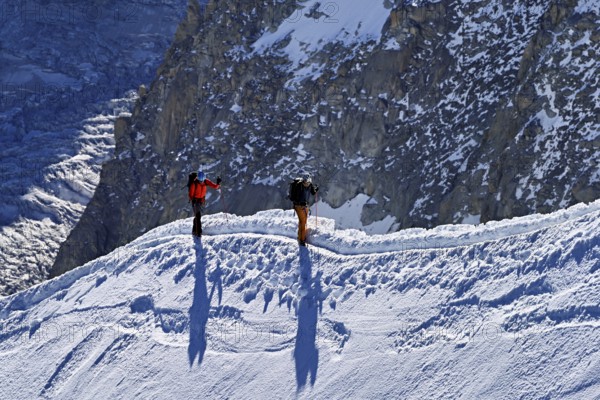 Two mountaineers run across a snow-covered mountain ridge, Aiguille du Midi, Chamonix-Mont-Blanc, Haute-Savoie, France