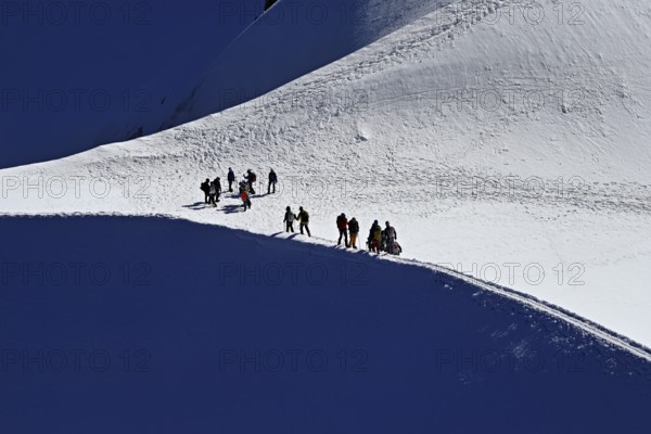 A group of mountaineers runs across a snow-covered mountain ridge, Aiguille du Midi, Chamonix-Mont-Blanc, Haute-Savoie, France