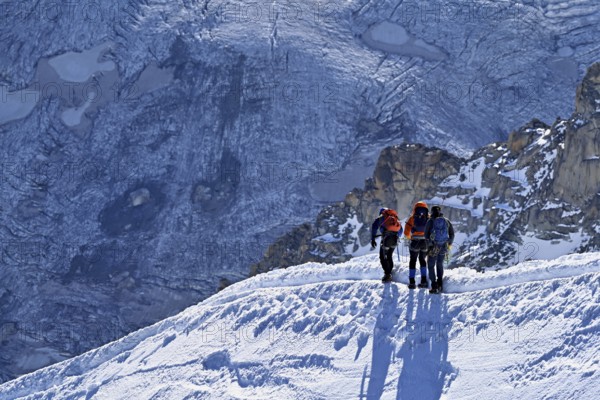 Three ascended mountaineers run across a snow-covered mountain ridge, Aiguille du Midi, Chamonix-Mont-Blanc, Haute-Savoie, France