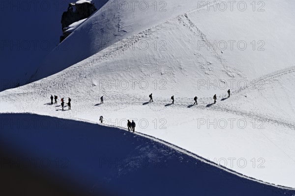 A group of mountaineers runs across a snow-covered mountain, Aiguille du Midi, Chamonix-Mont-Blanc, Haute-Savoie, France