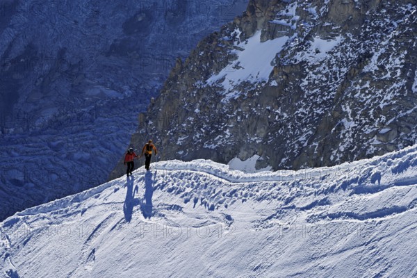Two ascended mountaineers run across a snow-covered mountain ridge, Aiguille du Midi, Chamonix-Mont-Blanc, Haute-Savoie, France
