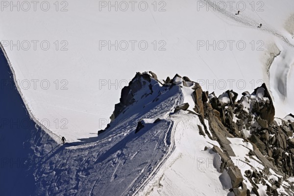 A mountaineer climbs over a snow-covered mountain ridge, Aiguille du Midi, Chamonix-Mont-Blanc, Haute-Savoie, France