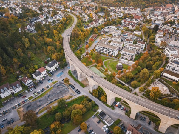 Aerial view of a city with a curved bridge surrounded by autumn trees and residential buildings, Nagold, Black Forest, Germany