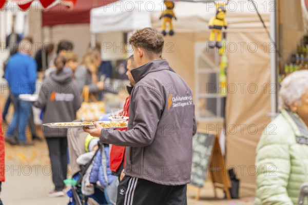 Person with tray serving food at a busy market while visitors look at the stalls, Streuobstmarkt, Sindelfingen, Böblingen district, Germany