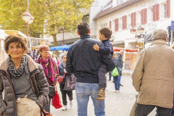 Visitors in autumn clothes stroll while a man carries a child, Streuobstmarkt, Sindelfingen, Böblingen district, Germany