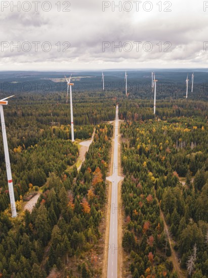 Several wind power plants along a road in a large autumn forest, Simmersfeld wind farm, Germany