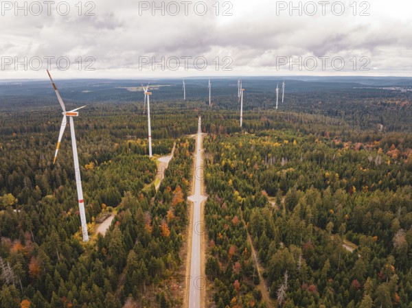 Wind turbines along a long road through an autumnal forest, Simmersfeld wind farm, Germany