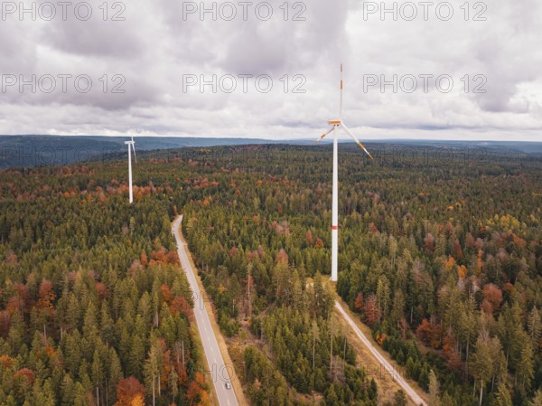 Wind turbines in colorful autumn forest with road under cloudy sky, Simmersfeld wind farm, Germany