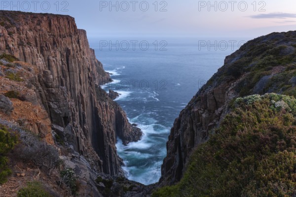 The Gap with long exposure shows the sunset over the cliffs of Cape Raoul. Golden light hits the sea and colors the rocks warmly in the evening. Cape Raoul, Tasman Peninsula, Tasmania, Australia